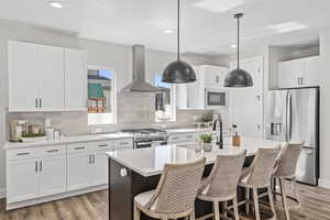 Kitchen featuring appliances with stainless steel finishes, decorative light fixtures, exhaust hood, and white cabinets