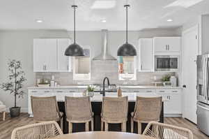 Kitchen featuring exhaust hood, stainless steel refrigerator with ice dispenser, hanging light fixtures, and built in microwave