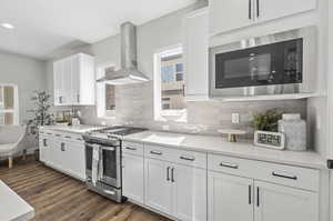 Kitchen featuring stainless steel appliances, wall chimney range hood, white cabinets, and dark hardwood / wood-style floors