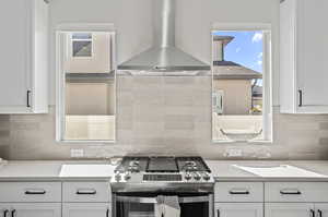 Kitchen with wall chimney exhaust hood, stainless steel gas range, and white cabinetry