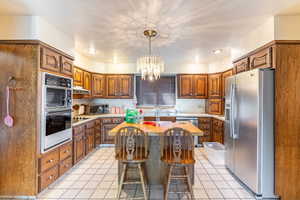 Kitchen with light tile patterned floors, sink, a kitchen island, a chandelier, and black appliances