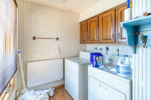 Clothes washing area with separate washer and dryer, light tile patterned floors, and cabinets