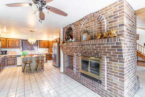 Kitchen featuring appliances with stainless steel finishes, hanging light fixtures, a brick fireplace, a breakfast bar, and a center island