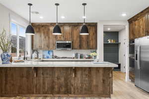 Kitchen with kitchen peninsula, light wood-type flooring, stainless steel appliances, sink, and pendant lighting