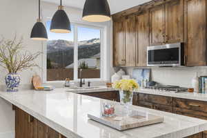 Kitchen featuring a mountain view, hanging light fixtures, tasteful backsplash, light stone counters, and stainless steel appliances
