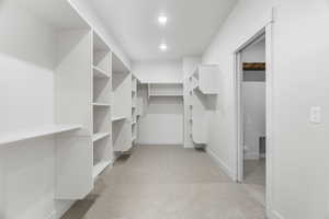 Walk in primary closet featuring built-in shelving and private entry to laundry room
