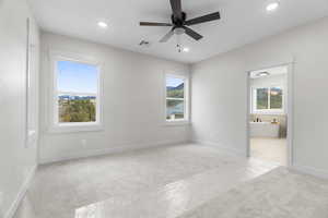 Primary bedroom featuring ensuite bath, ceiling fan, and light carpet