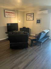 Living room featuring a textured ceiling, a wall mounted air conditioner, and dark hardwood / wood-style flooring