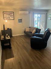 Living room featuring a textured ceiling, dark wood-type flooring, and a wall mounted AC