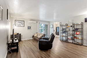 Living room featuring hardwood / wood-style floors, a wall mounted AC, and a textured ceiling