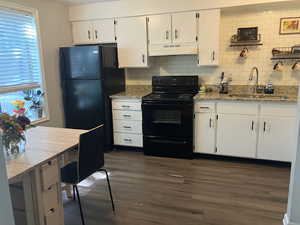 Kitchen with dark wood-type flooring, sink, light stone countertops, white cabinets, and black appliances