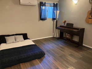 Bedroom with a wall unit AC and dark wood-type flooring