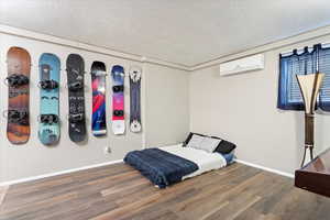 Bedroom featuring hardwood / wood-style floors, an AC wall unit, and a textured ceiling