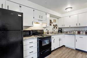 Kitchen with light hardwood / wood-style flooring, backsplash, black appliances, light stone countertops, and white cabinets