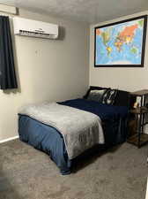 Bedroom featuring dark carpet, a wall unit AC, and a textured ceiling