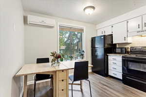 Kitchen featuring black appliances, light wood-type flooring, an AC wall unit, white cabinetry, and decorative backsplash