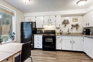 Kitchen with light hardwood / wood-style floors, white cabinets, black appliances, and sink