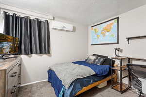 Carpeted bedroom featuring a textured ceiling and a wall mounted air conditioner