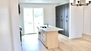 Kitchen featuring light wood-type flooring, sink, light brown cabinets, a center island with sink, and a notable chandelier