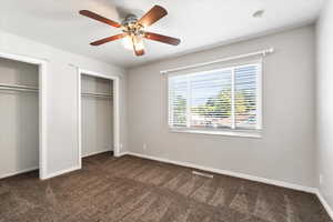 Unfurnished bedroom with ceiling fan, dark carpet, and two closets