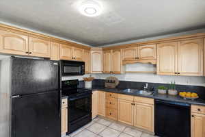 Kitchen: light tile patterned floors, black appliances, sink, and bright cabinets