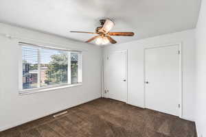 Unfurnished bedroom with dark carpet and ceiling fan