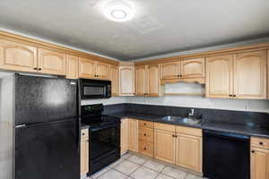 Kitchen: light tile patterned floors, light brown cabinets, sink, and black appliances