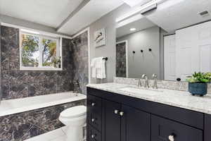 Full bathroom featuring vanity, tiled shower / bath combo, tile patterned flooring, a textured ceiling, and toilet