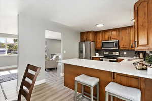 Kitchen with a breakfast bar area, light hardwood / wood-style flooring, kitchen peninsula, backsplash, and appliances with stainless steel finishes