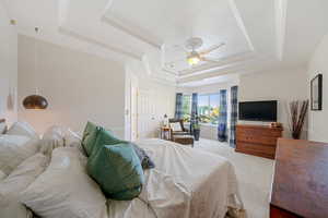 Carpeted bedroom featuring a raised ceiling, ornamental molding, and ceiling fan