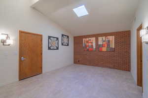 Unfurnished room with brick wall and lofted ceiling with skylight