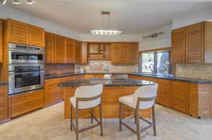 Kitchen featuring a kitchen island, sink, backsplash, double oven, and a kitchen bar