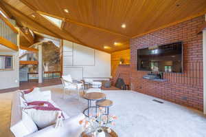 Carpeted living room featuring brick wall, lofted ceiling with skylight, and wooden ceiling