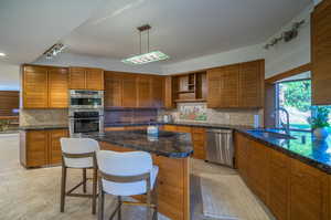 Kitchen with a kitchen island, sink, decorative backsplash, hanging light fixtures, and appliances with stainless steel finishes