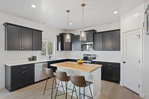 Kitchen featuring light wood-type flooring, a kitchen island, sink, hanging light fixtures, and appliances with stainless steel finishes