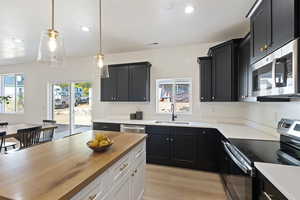 Kitchen with stainless steel appliances, wooden counters, sink, light hardwood / wood-style floors, and pendant lighting