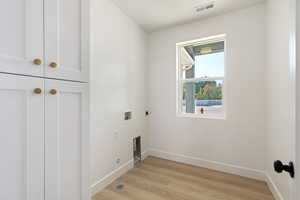 Clothes washing area featuring hookup for a washing machine, cabinets, light hardwood / wood-style floors, and hookup for an electric dryer