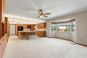 Kitchen with ceiling fan, a breakfast bar, light carpet, sink, and black appliances