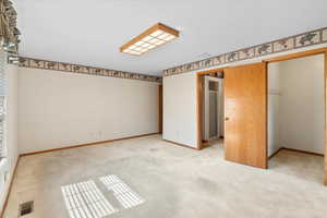 Unfurnished bedroom featuring light carpet, a spacious closet, and a closet