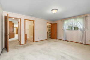 Unfurnished bedroom featuring a spacious closet, a closet, light colored carpet, and ensuite bathroom