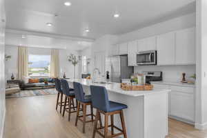 Kitchen with an island with sink, stainless steel appliances, sink, light hardwood / wood-style floors, and white cabinetry