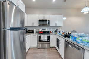 Kitchen featuring light stone counters, decorative light fixtures, white cabinetry, appliances with stainless steel finishes, and light hardwood / wood-style floors