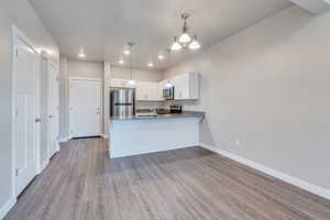 Kitchen with white cabinets, kitchen peninsula, pendant lighting, stainless steel appliances, and light wood-type flooring