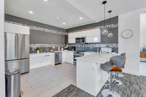 Kitchen with appliances with stainless steel finishes, white cabinets, kitchen peninsula, a textured ceiling, and decorative light fixtures