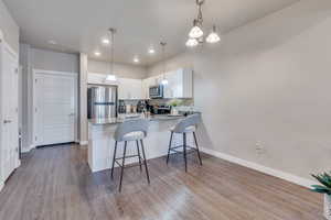 Kitchen with kitchen peninsula, white cabinetry, stainless steel appliances, light stone countertops, and light hardwood / wood-style floors