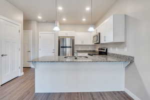 Kitchen with appliances with stainless steel finishes, kitchen peninsula, sink, and decorative light fixtures