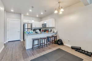 Kitchen featuring light wood-type flooring, white cabinets, kitchen peninsula, stainless steel appliances, and light stone countertops