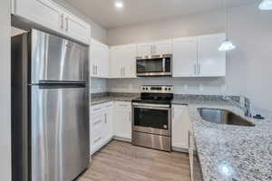 Kitchen with light wood-type flooring, light stone counters, sink, white cabinets, and stainless steel appliances