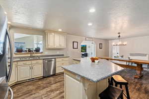 Kitchen with cream cabinetry, dark wood-type flooring, sink, hanging light fixtures, and appliances with stainless steel finishes