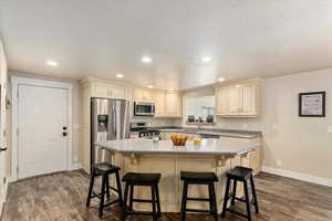 Kitchen featuring a textured ceiling, a breakfast bar area, stainless steel appliances, and dark hardwood / wood-style flooring